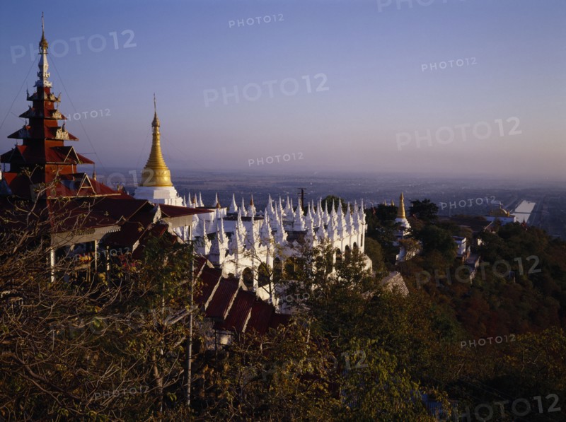 MYANMAR, Mandalay, View south from Mandalay Hill over temple stupas and pagoda style roof.