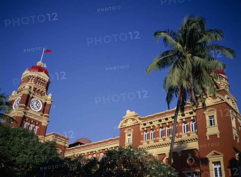 MYANMAR, Yangon, Part view of exterior of historic post office building and clock tower with palm tree in foreground.