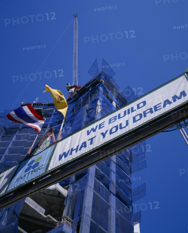THAILAND, Bangkok, Looking up at sign ‘We Build What You Dream’ with high rise building under construction behind.
