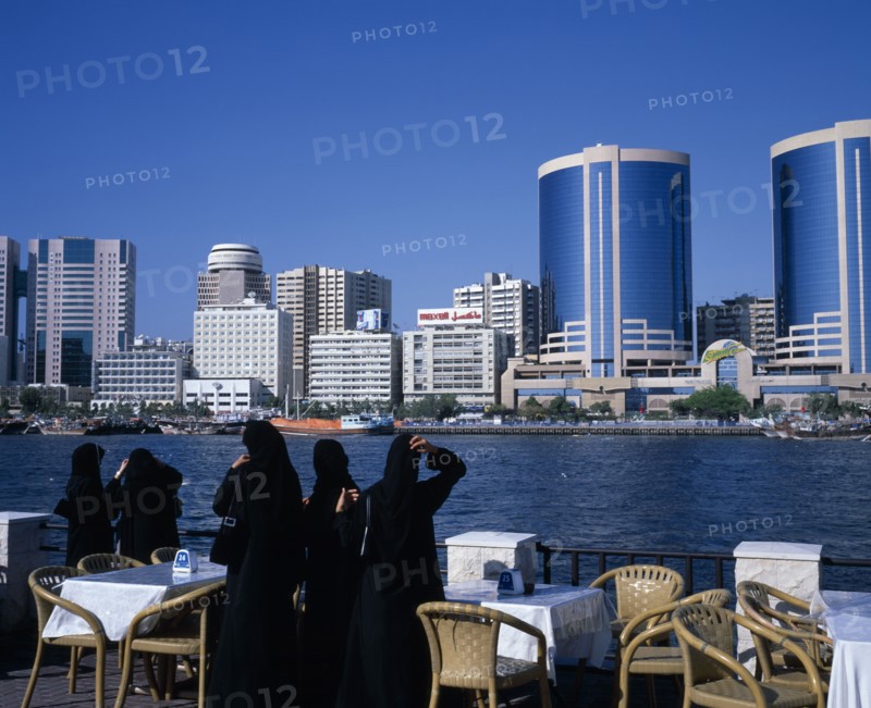 UAE, Dubai, Dubai Creek.  Women in waterfront restaurant on Bur Dubai city side looking out towards city skyline on Deira side.