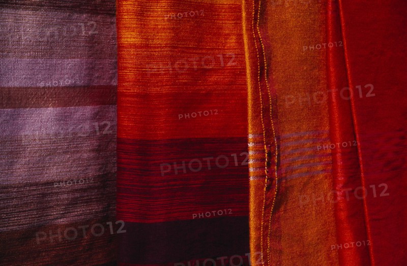 MOROCCO, Essaouira, Detail of red  orange and pale purple / blue woven textiles.