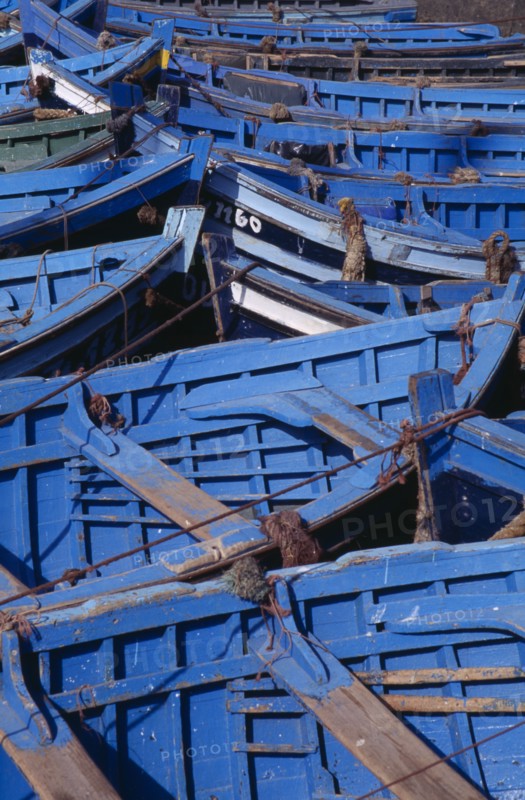 MOROCCO, Essaouira, Prows of blue and green fishing boats moored closely together.