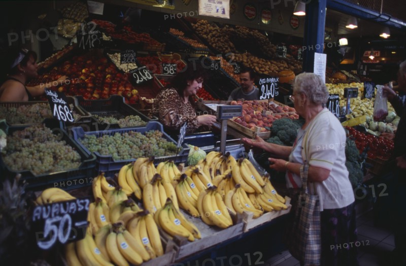 HUNGARY, Budapest, Fruit and vegetable stall in Central Market with woman customer and vendor making cash transaction. Eastern Europe