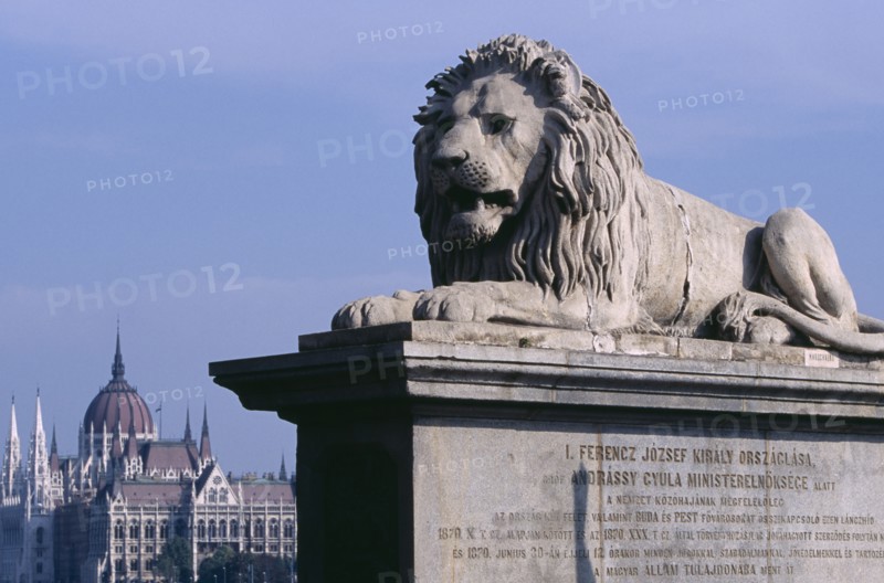 HUNGARY, Budapest, Stone statue of lion on Chain Bridge with Parliament building in distance behind. Eastern Europe