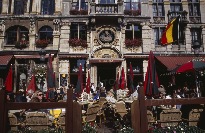 BELGIUM, Brabant, Brussels, Grand Place.  Busy cafe with people sitting at outside tables in the sunshine.  Part view of building facade with stone balcony and flower filled window boxes. UNESCO World Heritage Site