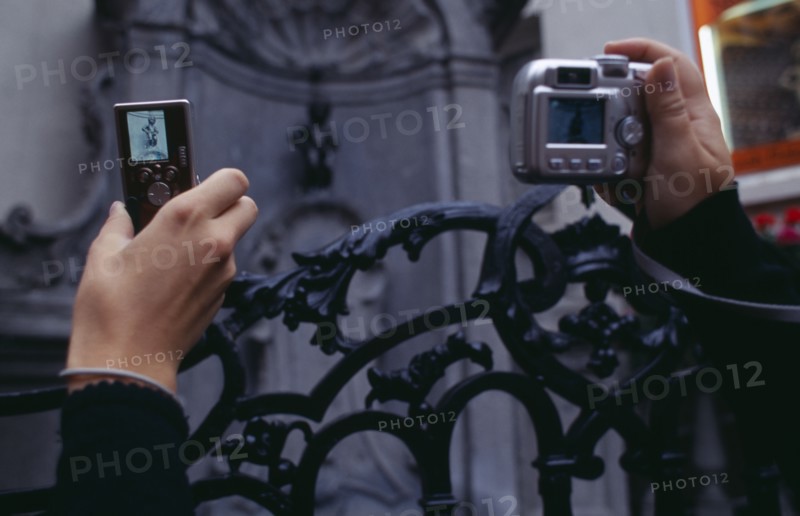 BELGIUM, Brabant, Brussels, Cropped view of visitors to the Manneken-Pis statue holding up digital camera and mobile phone to take photograph.