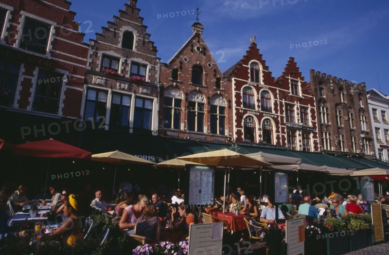 BELGIUM, West Flanders, Bruges, The Markt (Market Place)  Line of cafes with busy outside tables under green awnings and red umbrellas with menus displayed at side.