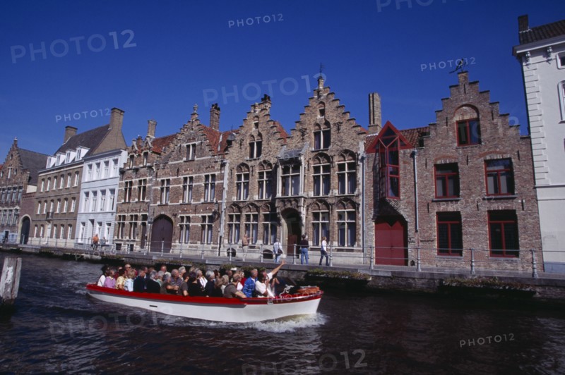 BELGIUM, West Flanders, Bruges, Tourist boat on canal with guide pointing out traditional waterside architecture.
