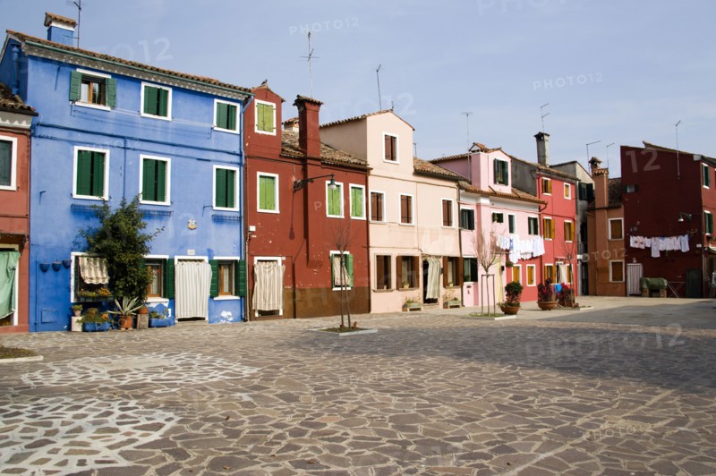 ITALY, Veneto, Venice, Colourful houses in a square on Burano. One of the few inhabited islands in the lagoon. Laundry hanging to dry outside windows.
