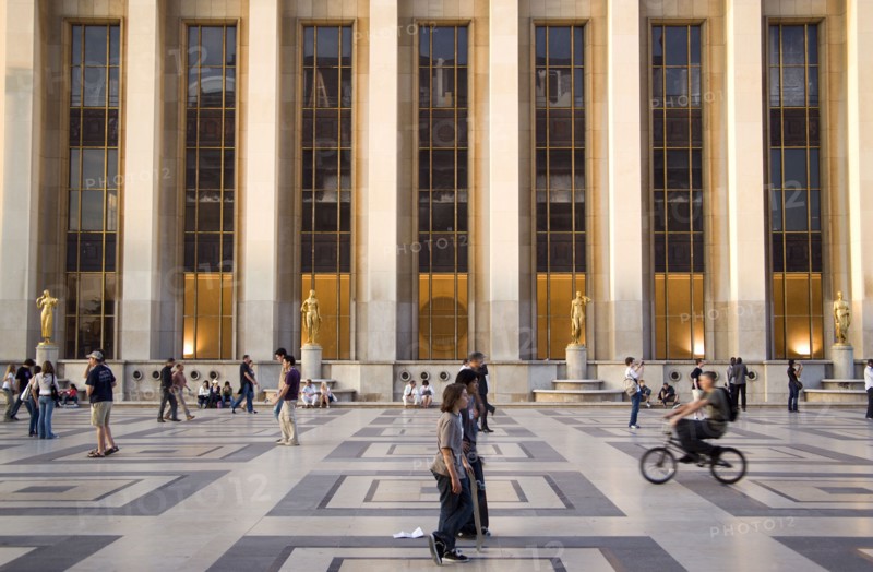FRANCE, Ile de France, Paris, Tourists beneath the gilded statues and the facade of the Theatre National de Chaillot in the central square of the Palais de Chaillot at sunset