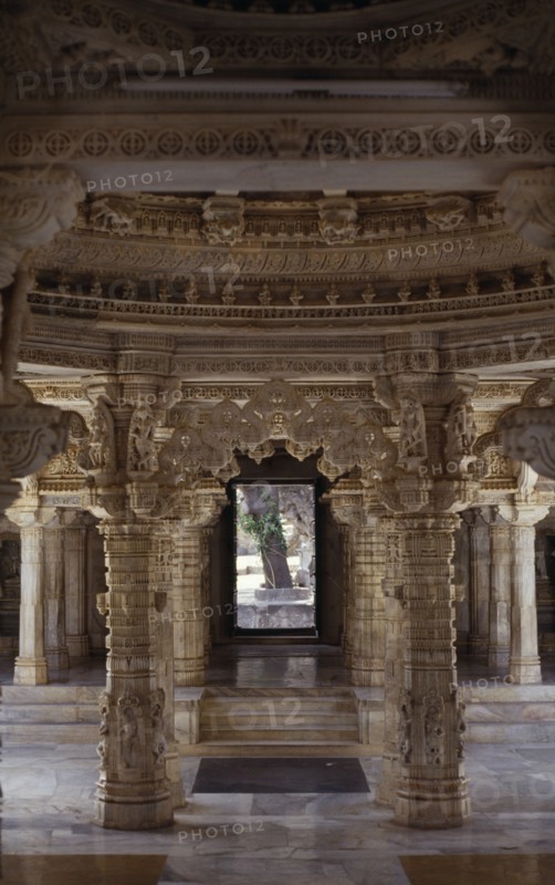 INDIA, Rajasthan, Mount Abu, Dilwara Temple complex dating from 11th-13th century A.D.  Detail of intricately carved white marble ceiling and supporting pillars framing view to outside courtyard.