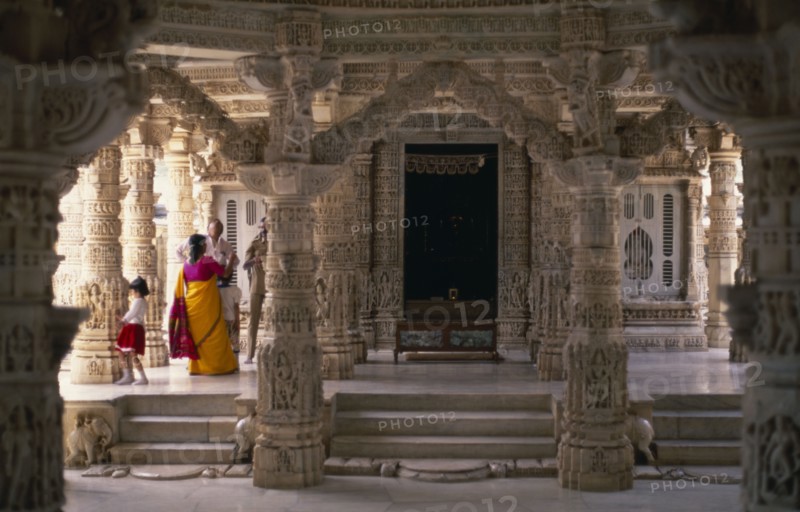INDIA, Rajasthan, Mount Abu, Dilwara Temples.  Vimal Vasahi 1031 A.D. Visitors on raised platform below intricately carved white marble ceiling and supporting pillars .