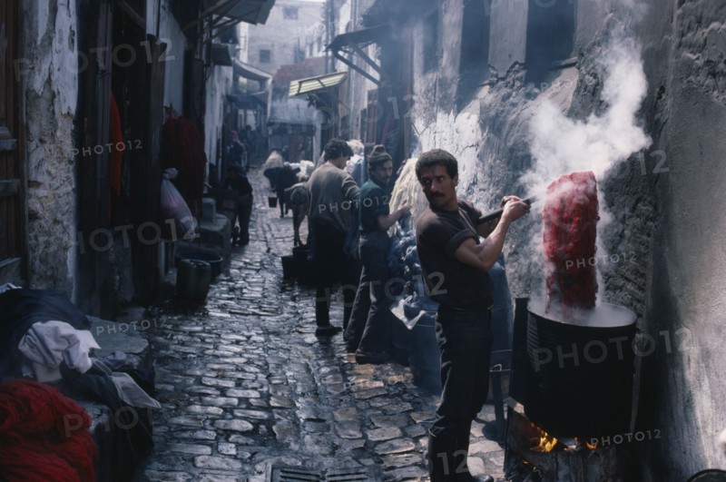 MOROCCO, Fez, Street in the wool dyeing souk with man in foreground lifting skein of yarn from vat of dye.