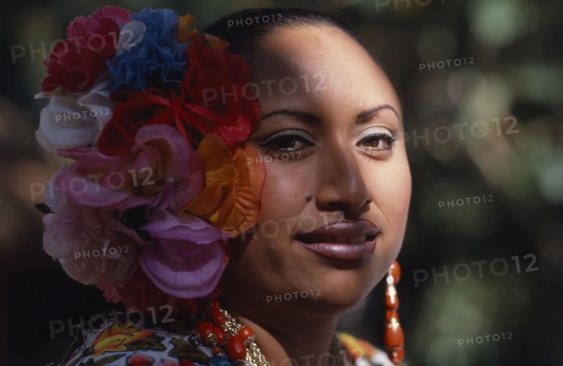 MEXICO, Yucatan, Chichen Itza, Head and shoulders portrait of female singer and dancer wearing silk flowers in her hair.