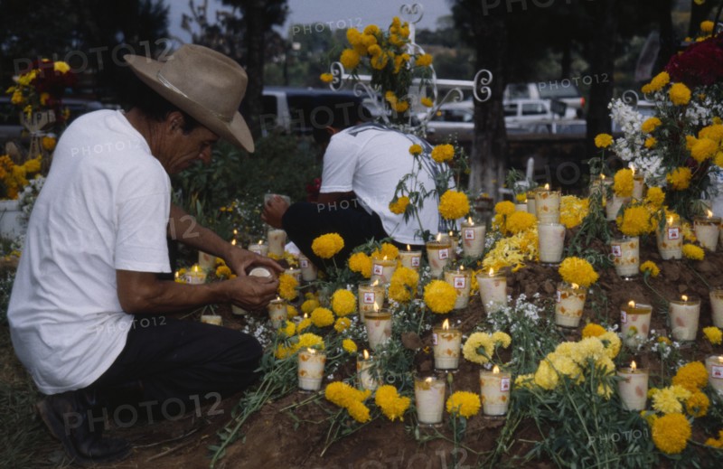 MEXICO, Michoacan, Purepecha, Tarascan Indian lighting candles on grave decorated with marigold flowers for Night of the Dead in Tzintzuntzan Cemetery.