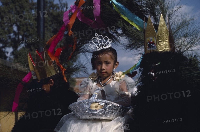 MEXICO, Tlaxcala, Little girl dressed in white flanked by two masked attendants in costume on float during carnival.