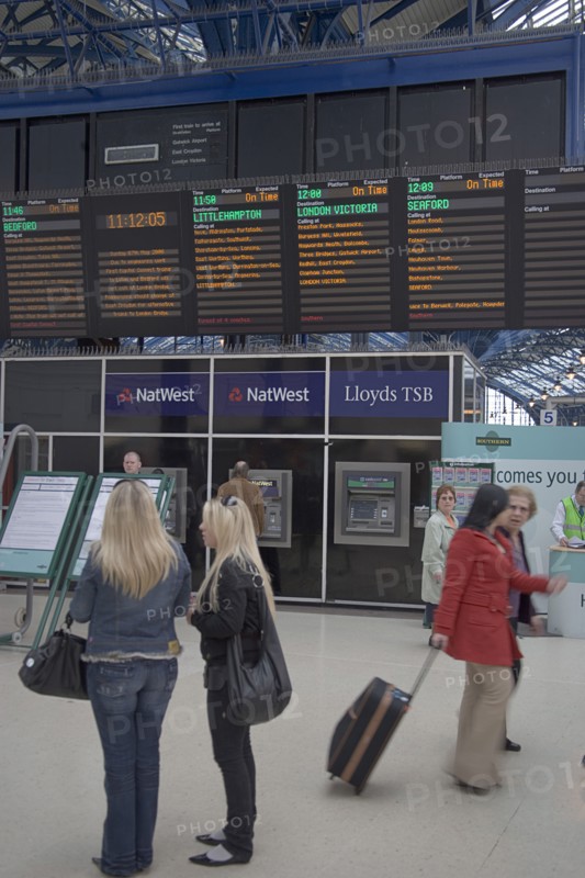 ENGLAND, East Sussex, Brighton, Passengers waiting by noticeboard at the central railway station.