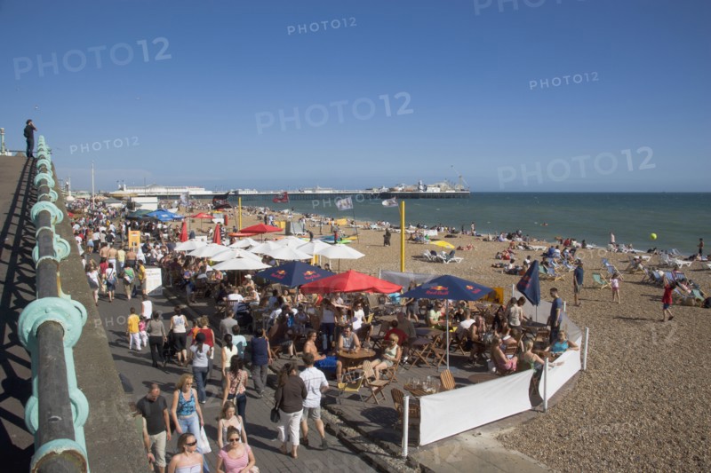 ENGLAND, East Sussex, Brighton, People sat at tables outside seafront bars and cafes.