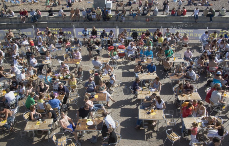 ENGLAND, East Sussex, Brighton, People sat at tables drinking outside the Beach seafront bar.