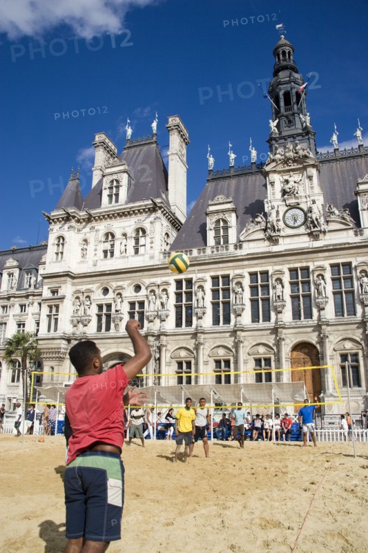FRANCE, Ile de France, Paris, The Paris Plage urban beach. Young people playing beach volleyball in front of the Hotel de Ville Town Hall with a young man serving