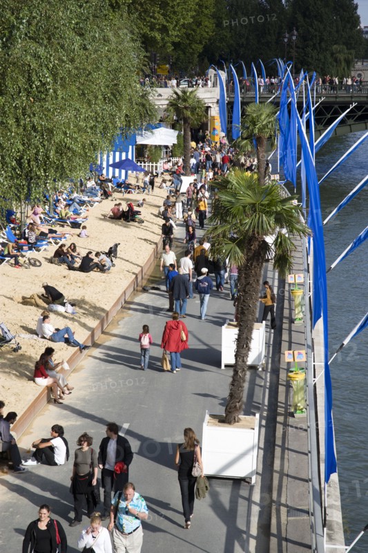 FRANCE, Ile de France, Paris, The Paris Plage urban beach. People strolling between the River Seine and other people lying on sand along the Voie Georges Pompidou usually a busy road now closed to traffic