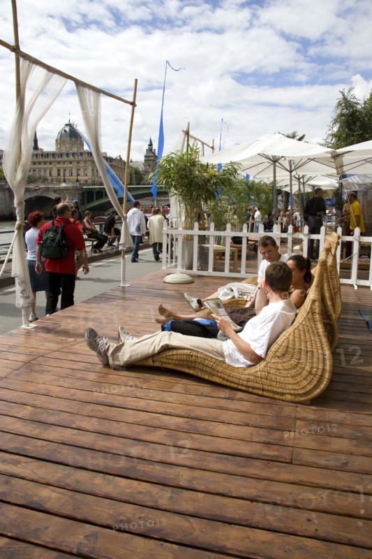 FRANCE, Ile de France, Paris, "The Paris Plage urban beach. People strolling between the River Seine and other people lying on whicker chairs along the Voie Georges Pompidou usually a busy road, now closed to traffic opposite the Ile de la Cite"