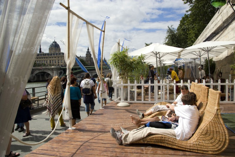 FRANCE, Ile de France, Paris, "The Paris Plage urban beach. People strolling between the River Seine and other people lying on whicker chairs along the Voie Georges Pompidou usually a busy road, now closed to traffic opposite the Ile de la Cite"