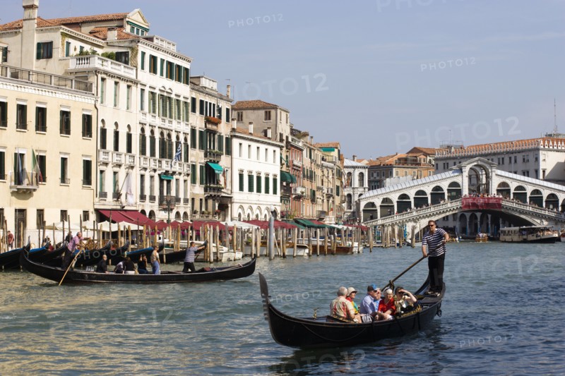 ITALY, Veneto, Venice, A Traghetto with local people on board crosses the Grand Canal and a Gondola carries tourists down river. Tourists crowd on the Rialto Bridge spanning the canal