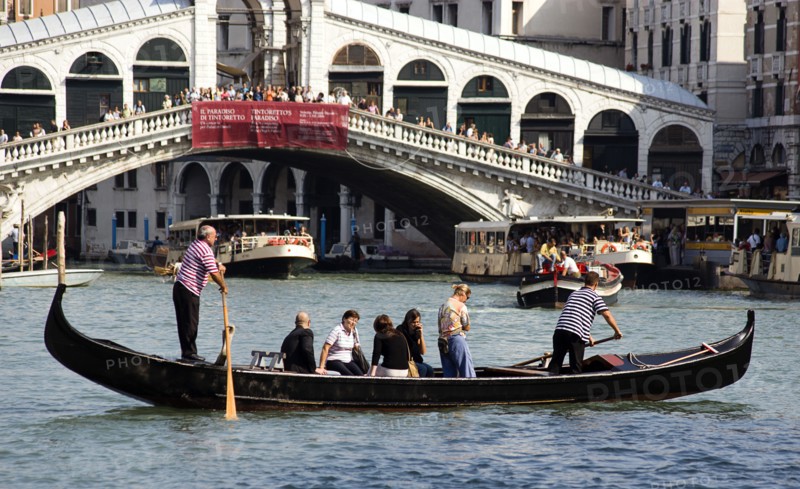 ITALY, Veneto, Venice, A Traghetto carrying local people on board crosses the Grand Canal. Tourists crowd on the Rialto Bridge spanning the canal with vaporetto passing beneath