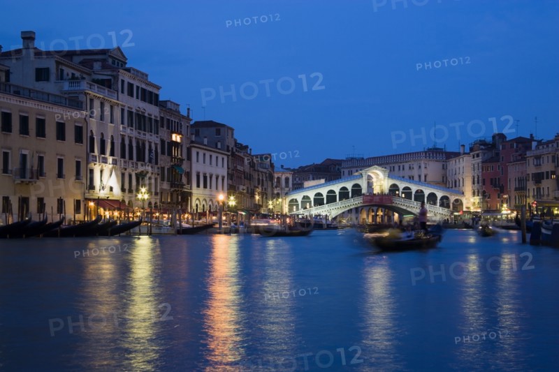 ITALY, Veneto, Venice, The Rialto Bridge spanning the Grand Canal illuminated at night with the canal busy with various water transport