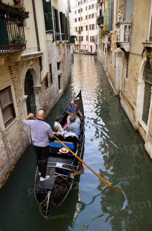 ITALY, Veneto, Venice, Gondolier carries sightseeing tourists in his gondola along a norrow canal in the San Marco disrtrict