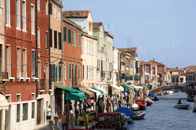 ITALY, Veneto, Venice, Tourists walking along the Fondamenta dei Vetrai with boats moored on the Rio dei Vetrai canal on the lagoon island of Murano