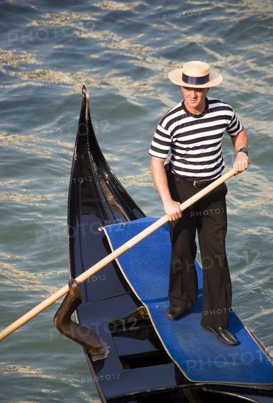 ITALY, Veneto, Venice, "A gondolier in traditional dress of beribboned straw hat, striped vest and black trousers on his gondola"