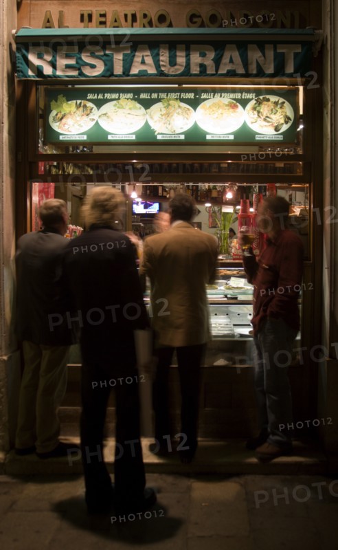 ITALY, Veneto, Venice, Men standing and eating at the street window of a restaurant near the Goldoni Theatre