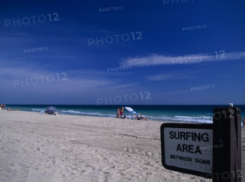 USA, Florida, Fort Lauderdale Beach, Designated Surfing Area Sign on sandy beach with sunbathers near the waters edge