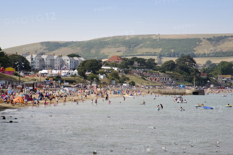 ENGLAND, Dorset, Swanage Bay, View across the sea towards the shoreline of sandy beach with sunbathers on the sand and swimming in the sea. Hotel buildings and hills behind.