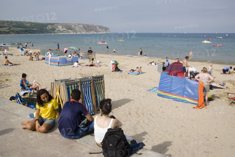 ENGLAND, Dorset, Swanage Bay, Busy sandy beach with sunbathers on the sand near deckchairs and windbreaks.