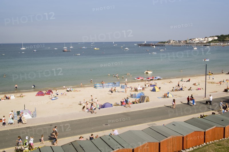 ENGLAND, Dorset, Swanage Bay, Elevated view over beach huts towards busy stretch of sandy beach and sea