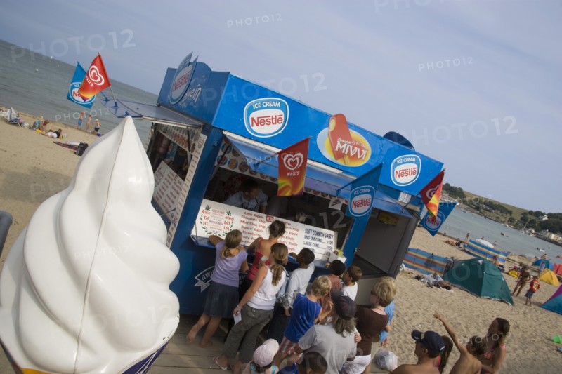 ENGLAND, Dorset, Swanage Bay, A group of children queuing at an Ice Cream stall. Angled view with a large plastic ice cream in the foreground.