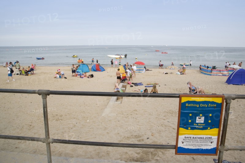 ENGLAND, Dorset, Swanage Bay, View through a railing with a Beach Safety sign towards busy sandy beach with sunbathers on the sand