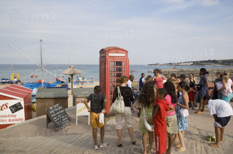 ENGLAND, Dorset, Swanage Bay, A group of children gathered near a traditional red phone box overlooking the beach