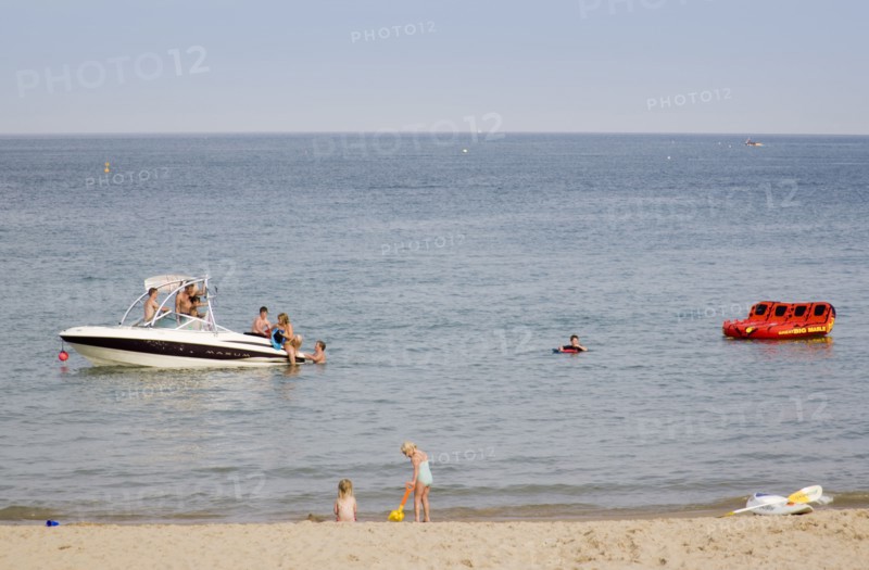 ENGLAND, Dorset, Swanage Bay, Children playing at the waters edge of a sandy beach with people on a speedboat on the sea