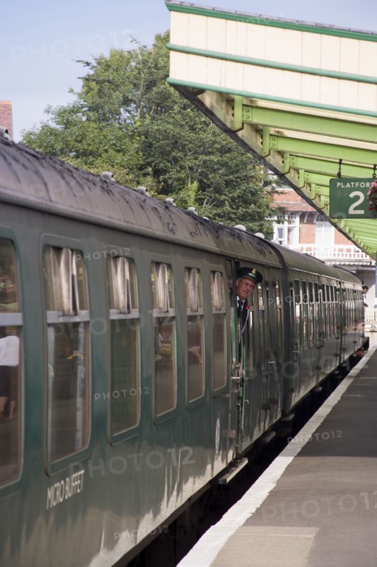ENGLAND, Dorset, Swanage, Steam Railway Station. View along platform with train departing from station and conductor seen looking out from carriages