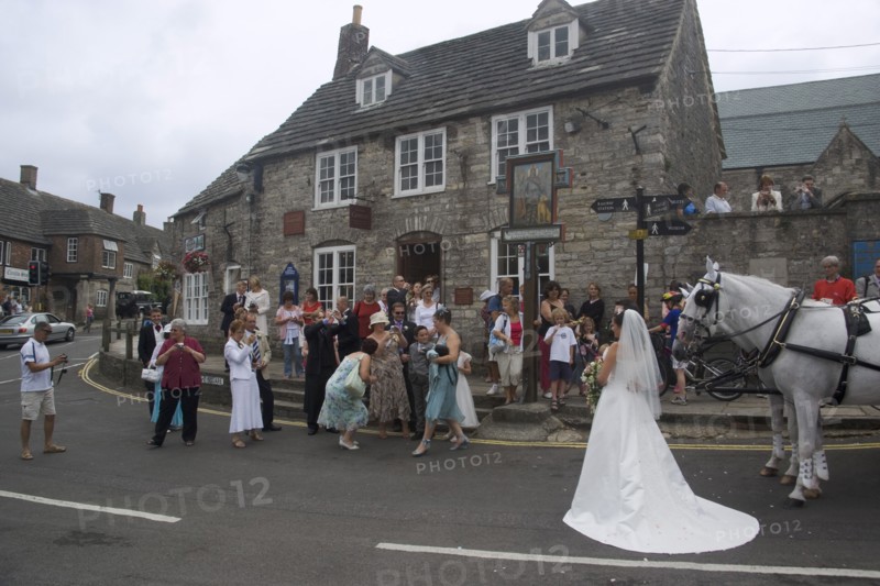 ENGLAND, Dorset, Corfe, A wedding party gathered on the street taking photographs of the bride near a shire horse