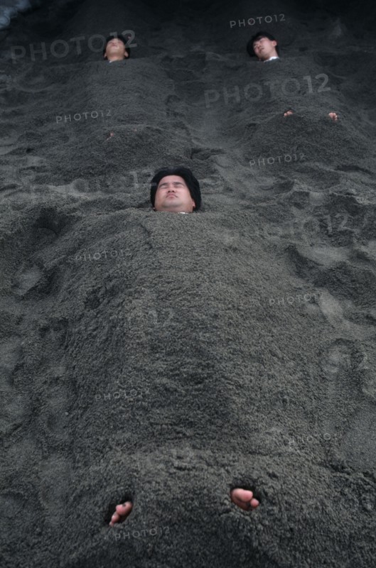 JAPAN, Kyushu, Ibusuki, Sunabulo. Hot Sand Bath with men submerged in sand with only heads and feet showing above surface