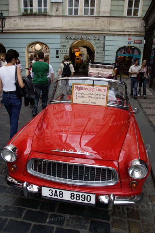 CZECH REPUBLIC, Bohemia, Prague, "Tourists walking past a red Skoda, parked in the street, used for sightseeing tours of the Old Town"