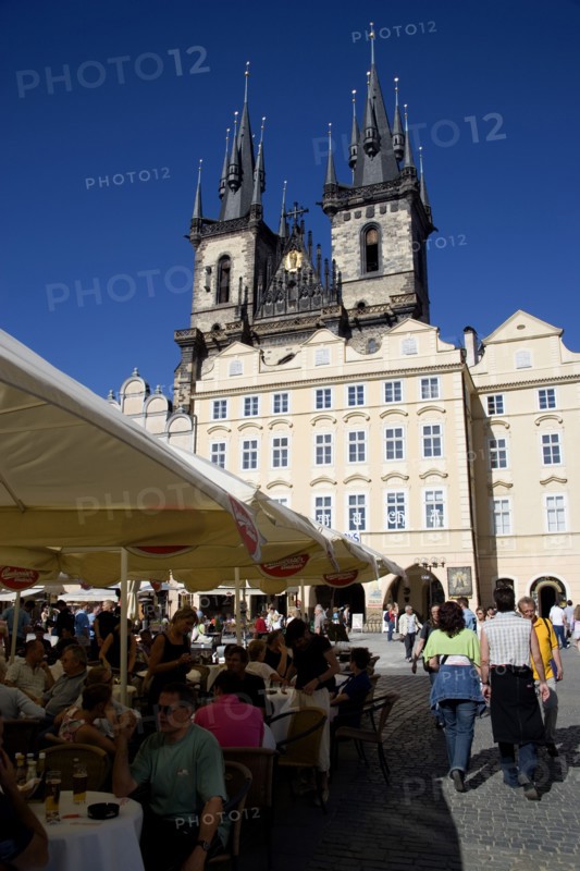CZECH REPUBLIC, Bohemia, Prague, The Old Town Square with the Church of Our Lady before Tyn. Tourists sit at tables under umbrellas outside cafes and restaurants whilst others stroll in the square
