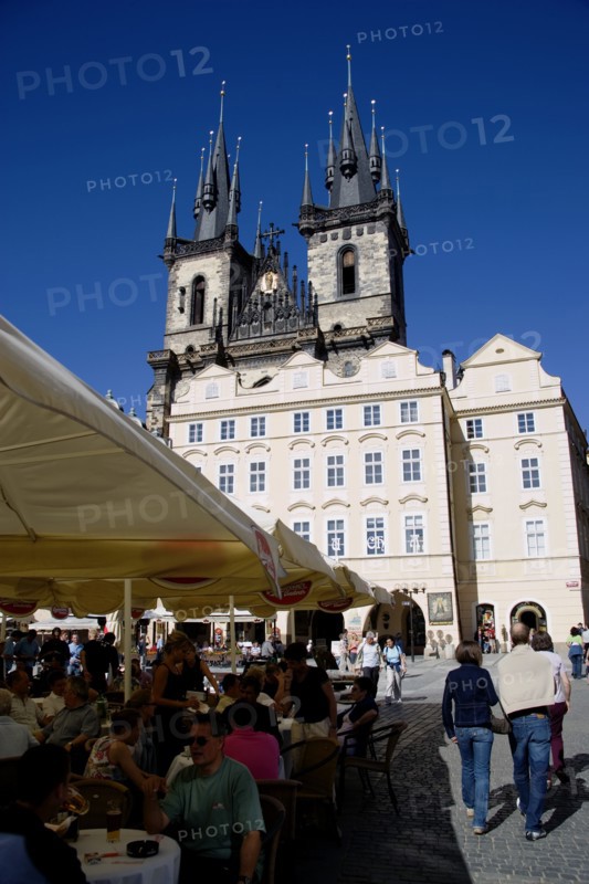 CZECH REPUBLIC, Bohemia, Prague, The Old Town Square with the Church of Our Lady before Tyn. Tourists sit at tables under umbrellas outside cafes and restaurants whilst others stroll in the square