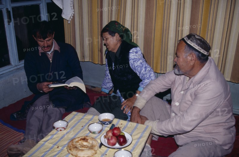 UZBEKISTAN, Tashkent, "Uzbek family sat around tablke, with one man reading a book."