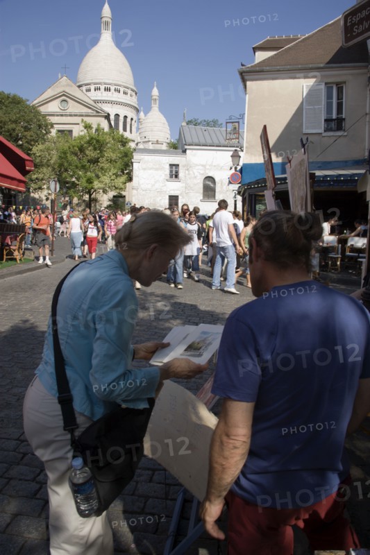 FRANCE, Ile de France, Paris, Montmartre Place du Tertre a square beside the church of Sacre Couer with a tourist discussing a painting with an artist vendor